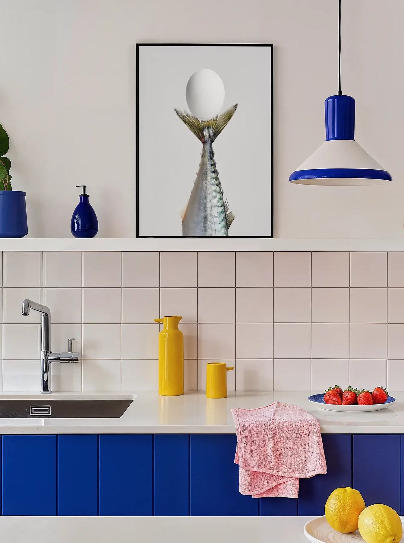 Interior view of a modern Scandinavian kitchen with blue cabinets and yellow accents, featuring the fine art print “Kaviar” by Monday Gallery. Printed in Sweden, exclusive at Monday Gallery.