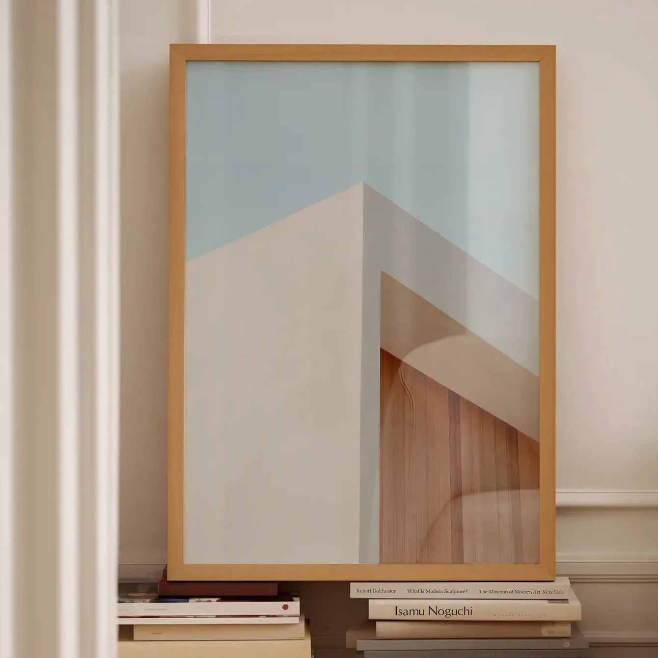 Framed fine art print “Architectural Harmony” by Monday Gallery, styled on a stack of design books against a neutral wall with soft daylight.