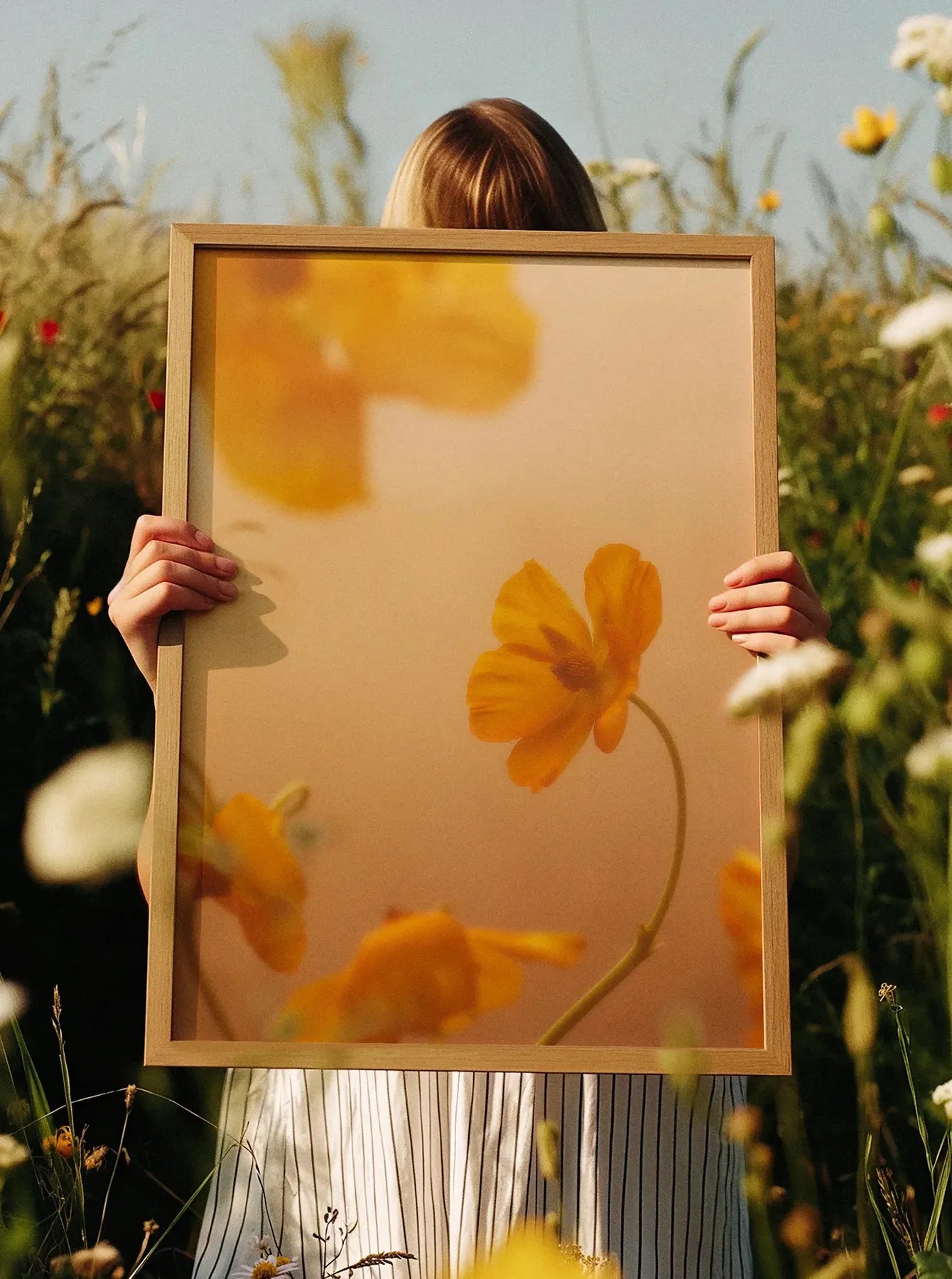 Framed fine art print “Golden Blooms” held outdoors in a sunlit field. Printed in Sweden, exclusive at Monday Gallery.