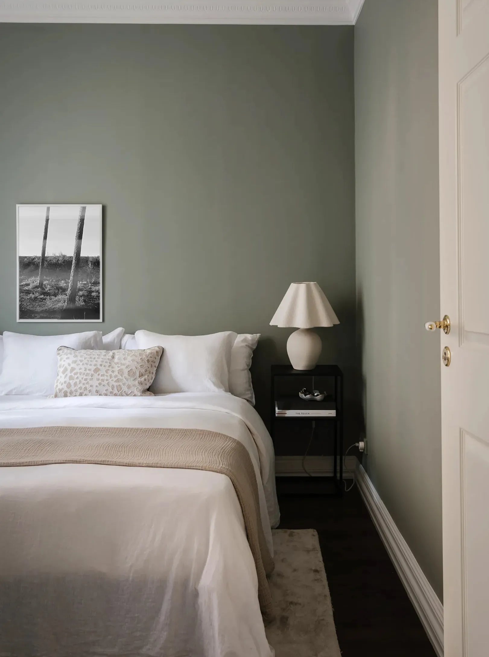 Framed black and white fine art print hanging above a neatly made bed in a minimalist Scandinavian bedroom with soft neutral tones.