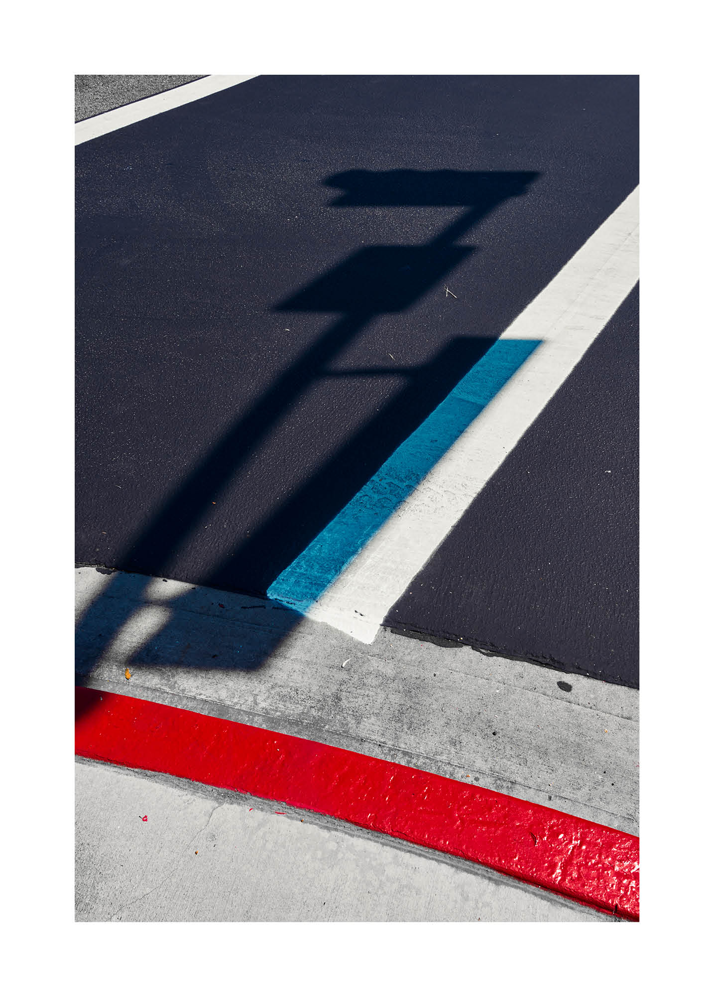 Minimalist fine art photograph of street markings in red, blue, and white with the shadow of a traffic sign.