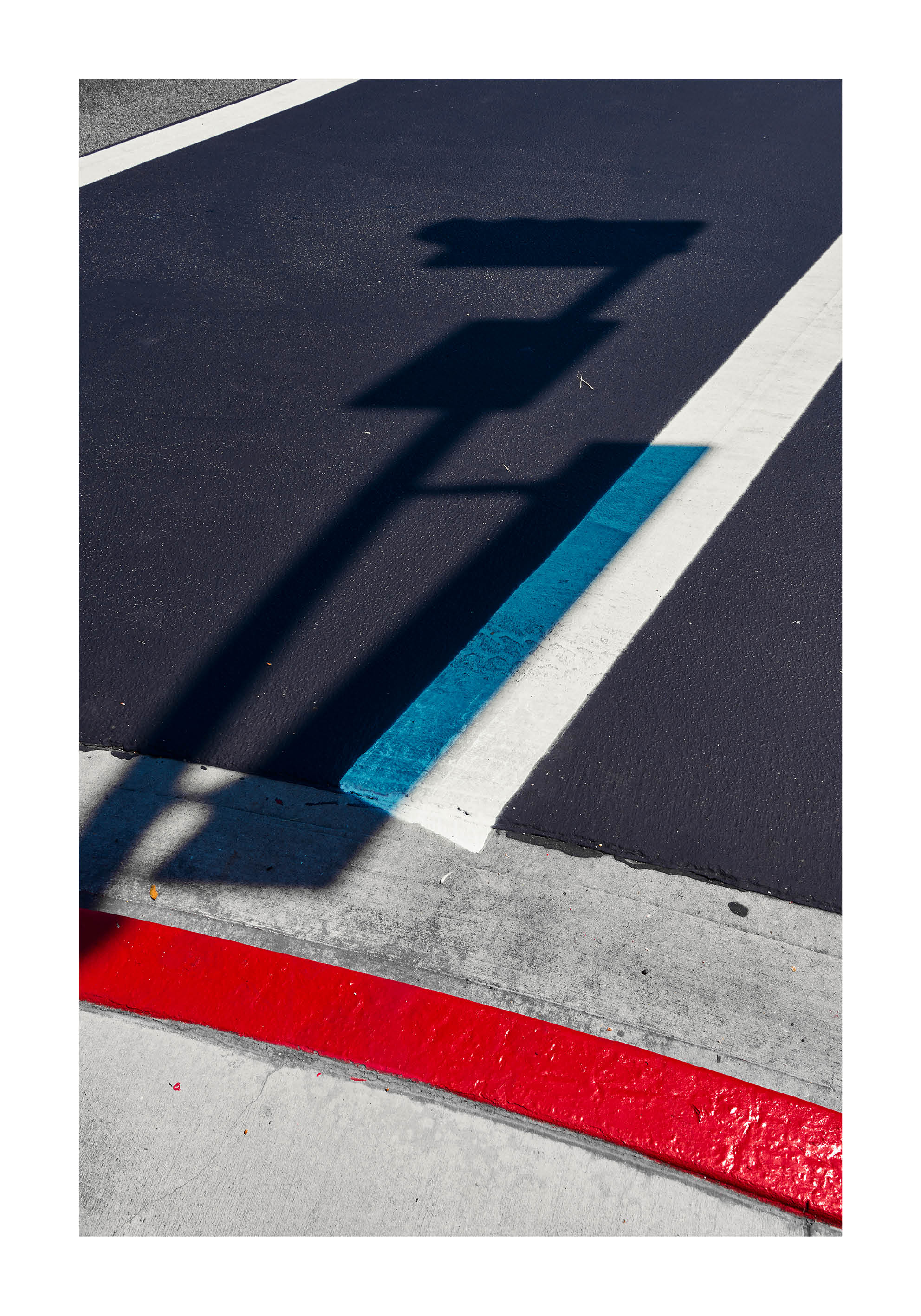 Minimalist fine art photograph of street markings in red, blue, and white with the shadow of a traffic sign.