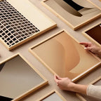 Collection of framed fine art prints from Monday Gallery, including “Beige Simplicity No.1”, arranged on a neutral surface with hands interacting.