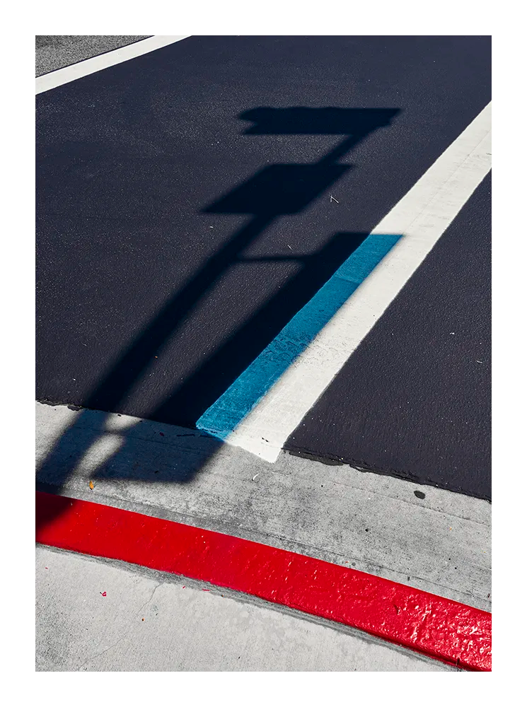 Minimalist fine art photograph of street markings in red, blue, and white with the shadow of a traffic sign.