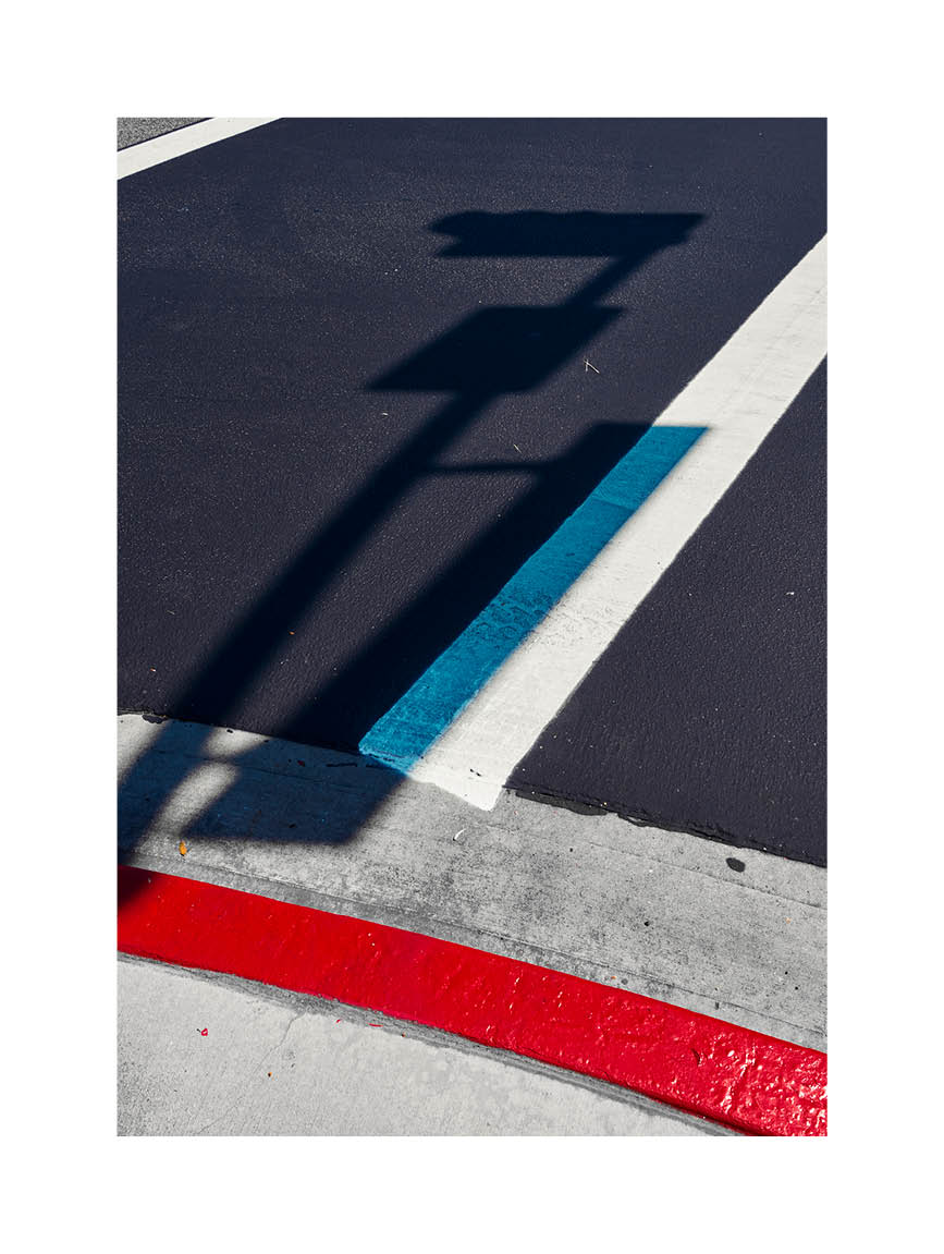 Minimalist fine art photograph of street markings in red, blue, and white with the shadow of a traffic sign.